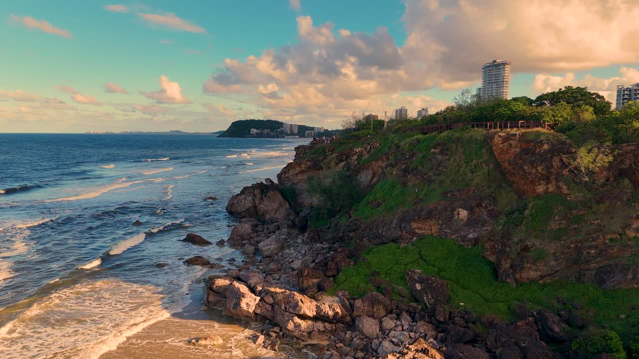 Drone footage captures Gold Coast's stunning coastline, showcasing rocky cliffs, sandy beaches, and urban skyline under vibrant skies