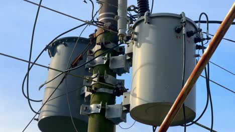 close-up footage of an electrical transformer mounted on a utility pole, surrounded by tangled high-voltage power lines under a clear blue sky