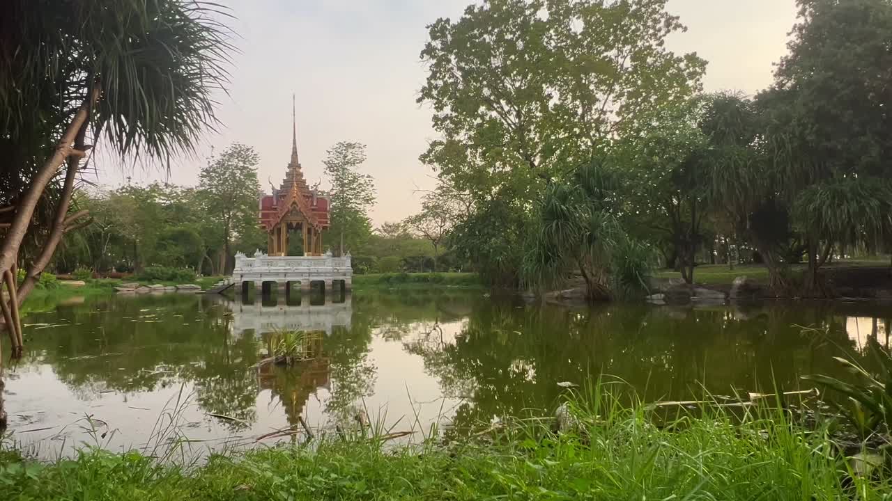 A stunning temple pavilion stands gracefully over a still pond, reflecting the surrounding greenery and the golden hues of the sky.