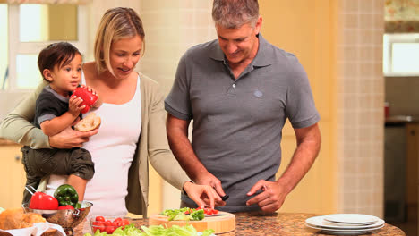 padre preparando verduras mientras la madre sostiene al bebé