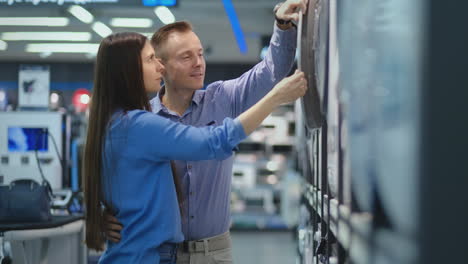 a handsome man and a woman choose a washing machine to buy open the door and inspect the coating of the drum and the quality of the product. a woman looks inside the washing machine. the purchase of a washing machine for home