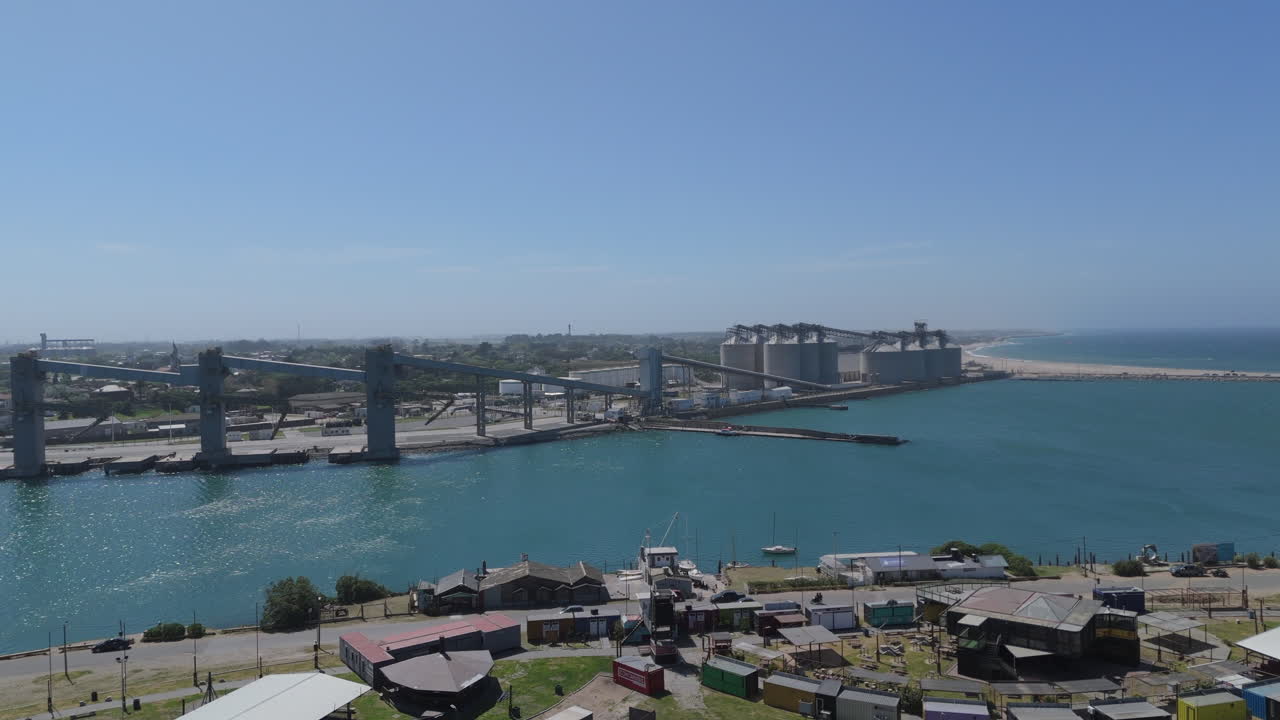 A busy port facility in Necochea, Argentina, with silos, cranes, and calm water visible
