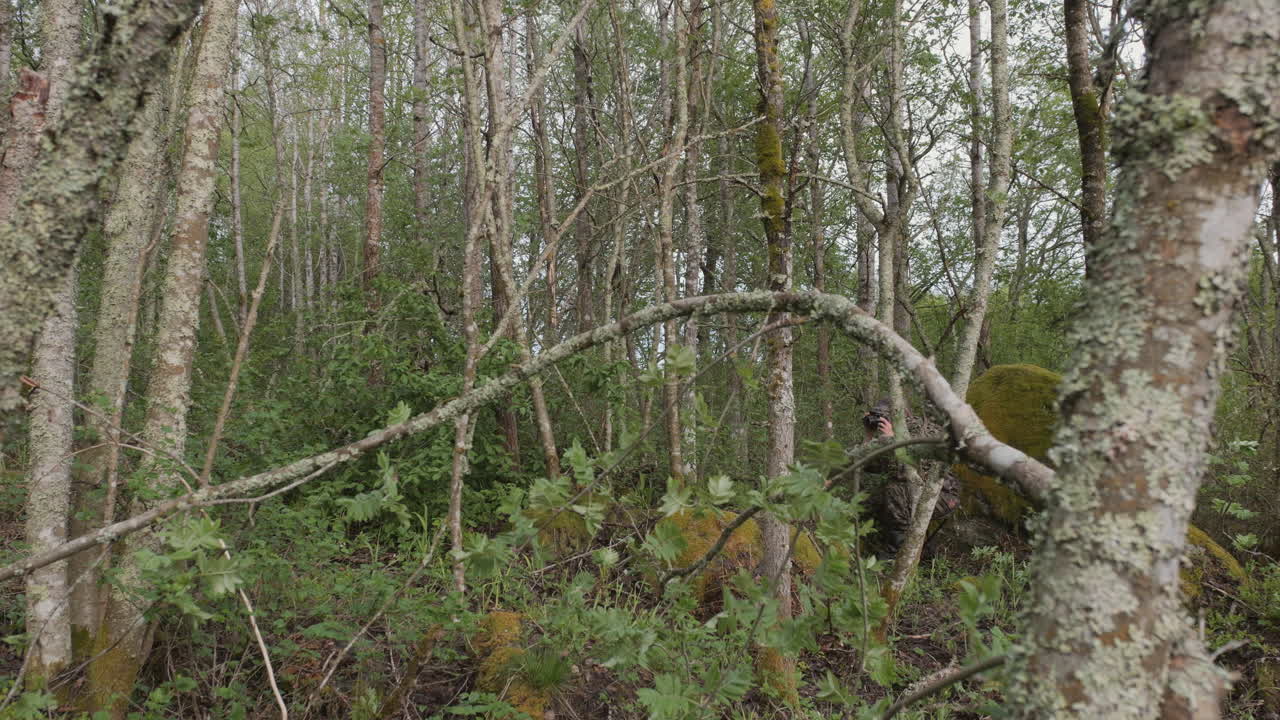 Uomo nascosto e camuffato con binocolo o fotocamera si nasconde e si confonde tra gli arbusti della foresta.