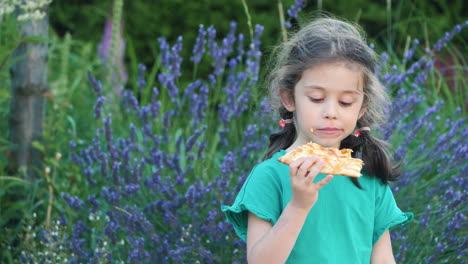 little girl eating pizza in a garden