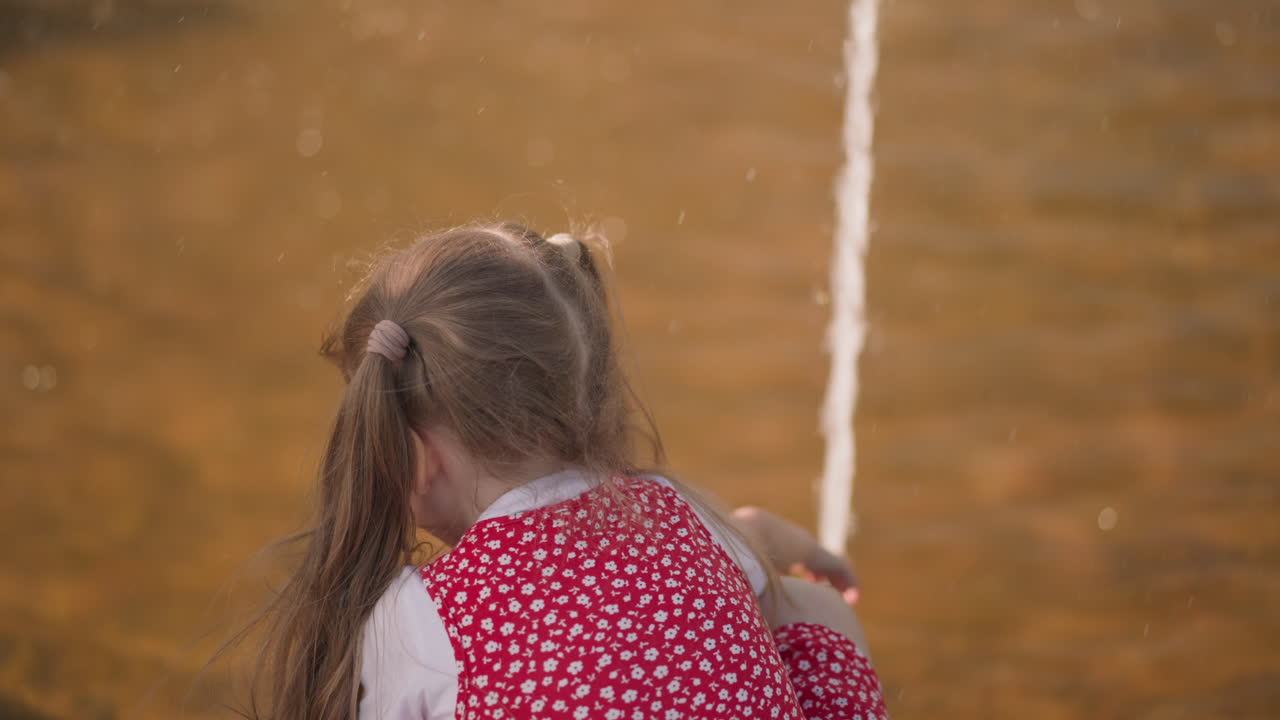 una niña rubia juega con agua de fuente en un parque urbano