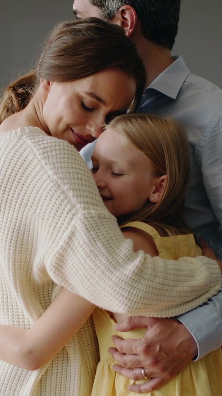 Vertical video: Leaning mom nestling while dad holding girl in studio with sweater, showing love