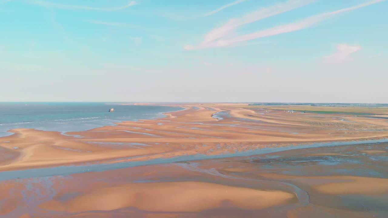 Drone footage captures the serene expanse of Holkham Beach in Norfolk at sunset, showcasing the pristine sand and vibrant sky from above. The scene is tranquil and devoid of people