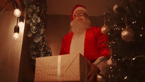 santa claus se inclina y pone una gran caja hermosa con un regalo para un buen niño debajo del árbol de navidad para el niño.
