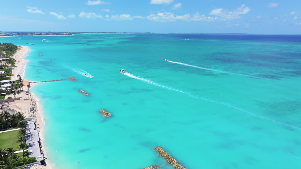 Curved forward wide shot starts from the land,  moving onto the clear blue waters and white sand beach with water activities, boats and jet skis creating dynamic splashes in the turquoise sea