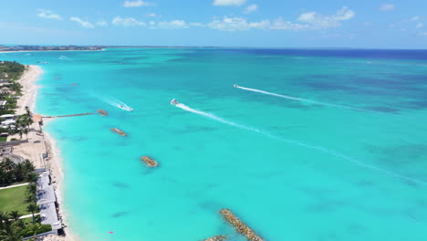 curved forward wide shot starts from the land,  moving onto the clear blue waters and white sand beach with water activities, boats and jet skis creating dynamic splashes in the turquoise sea