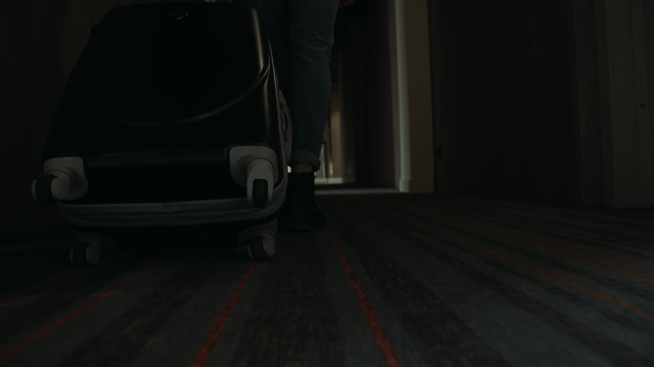 짐을 들고 복도를 따라 걸어가는 부츠를 입은 남자. 가방을 들고 있는 남자.