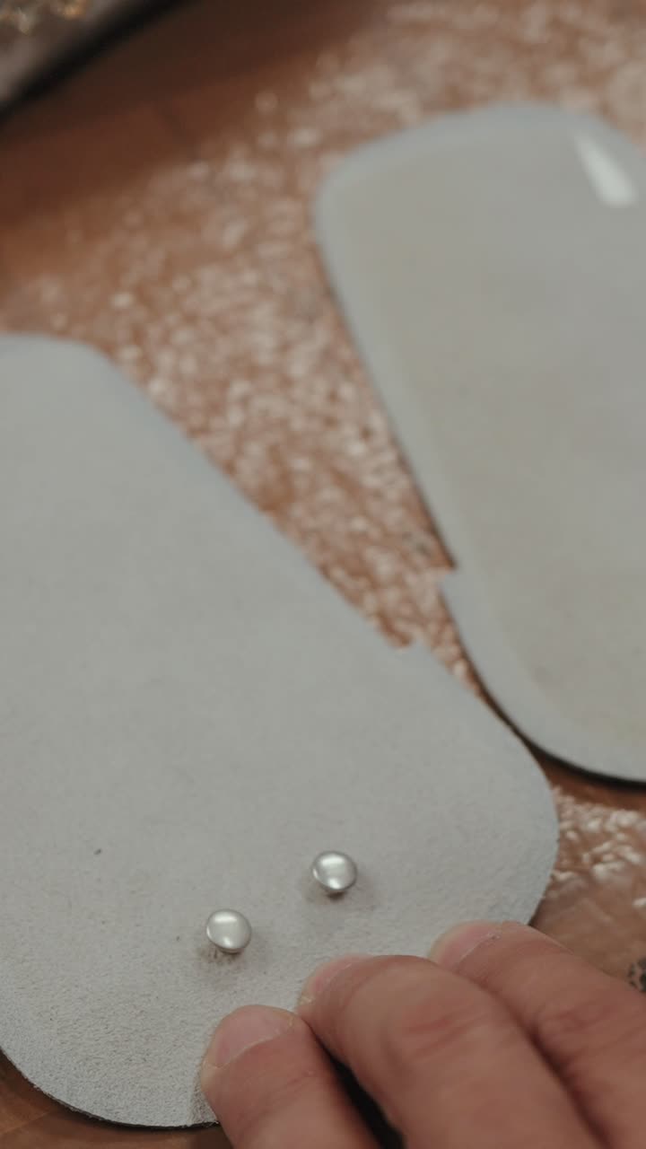 Vertical closeup of artisan setting metal studs on leather footwear part