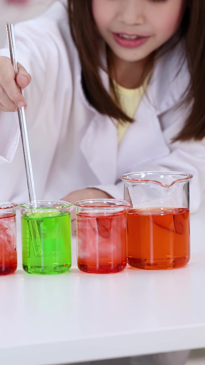 Uno studente in camice bianco mescola liquidi vivaci durante un esperimento scientifico.