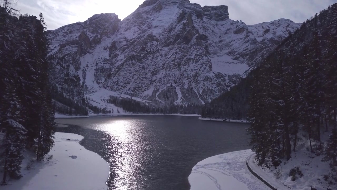 Lago ghiacciato circondato da cime montuose innevate e fitta foresta di conifere in inverno. Paesaggio alpino selvaggio che cattura condizioni climatiche fredde e terreno ghiacciato