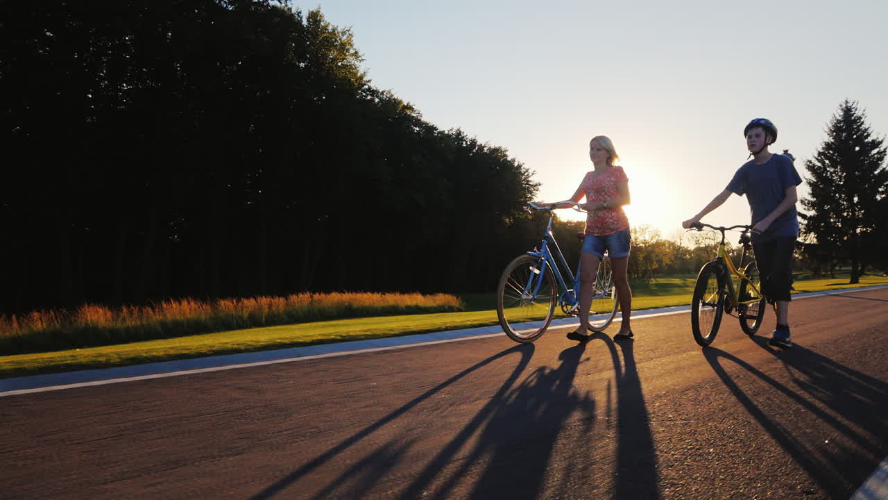 석양에 그녀의 아들 십대 리드 자전거와 함께 산책하는 여자