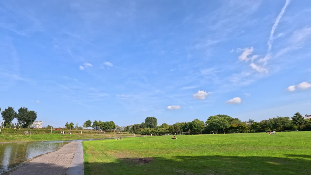 Wide daylight pan across Haarlem park, water, green grass, trees, blue sky, relaxed atmosphere