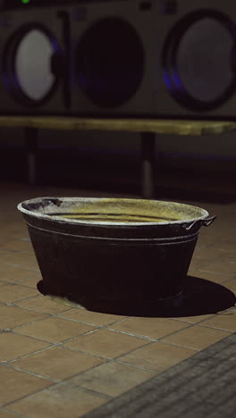 old black basin sits alone in an empty laundromat at night