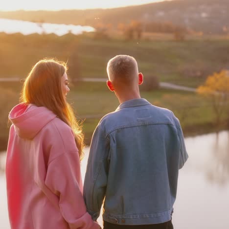 couple enjoys beautiful evening landscape in the countryside. young man and woman standing on the hill and looking on the river at sunset in autumn time