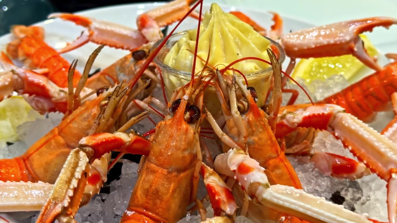 Primo piano di scampi arancioni vivaci disposti sul ghiaccio con spicchi di limone e una ciotola di salsa cremosa. Ideale per blog culinari o promozioni di ristoranti di pesce.