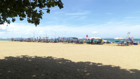 Imágenes-Frente-A-La-Playa-Tomadas-Bajo-Las-Sombras-De-Los-árboles-Que-Capturan-Una-Línea-De-Marquesinas-De-Playa-Con-Pancartas-Coloridas-Con-Vistas-Al-Mar-Y-Las-Montañas.