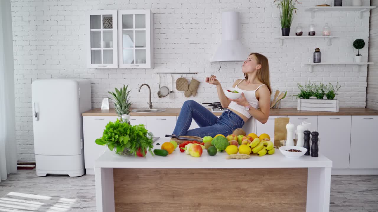 Happy woman eating vegan food. Modern kitchen background with fresh organic food on the table at home. Healthy lifestyle.