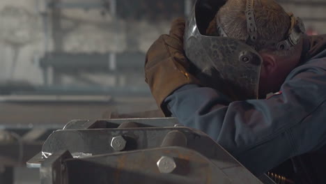 welder with mask connects metal details in plant workshop