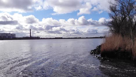 silhouetted industrial plant against cloudy sky by the calm river of oude maas near puttershoek town in netherlands