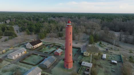 Luftaufnahme-Des-Roten-Akmenrags-Leuchtturms,-Ostseeküste,-Lettland,-Weißer-Sandstrand,-Ruhiges-Meer,-Sonniger-Tag-Mit-Wolken,-Weit-Entfernte-Drohnen-Umlaufaufnahme