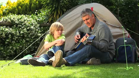 Hombre-Tocando-La-Guitarra-Con-Su-Hijo-Fuera-De-La-Tienda-En-El-Jardín