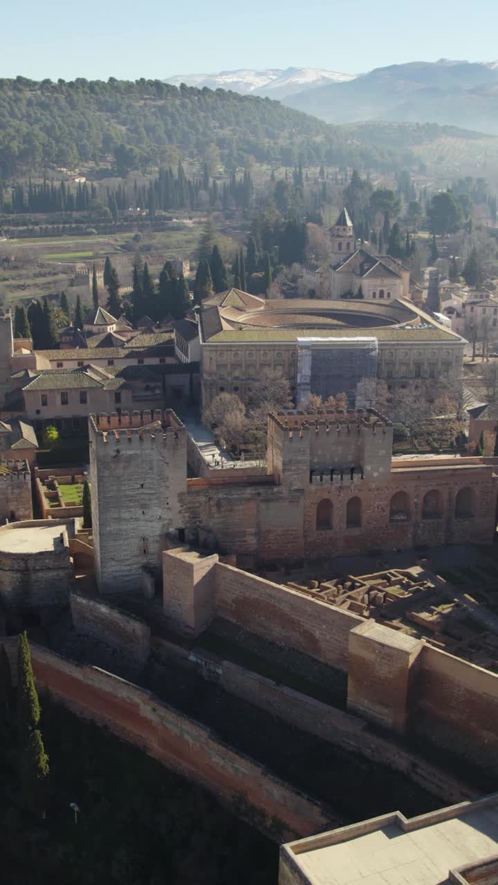 Drone aéreo vertical sobrevoando a fortaleza de Alhambra em Granada, Espanha, com montanhas cênicas ao fundo