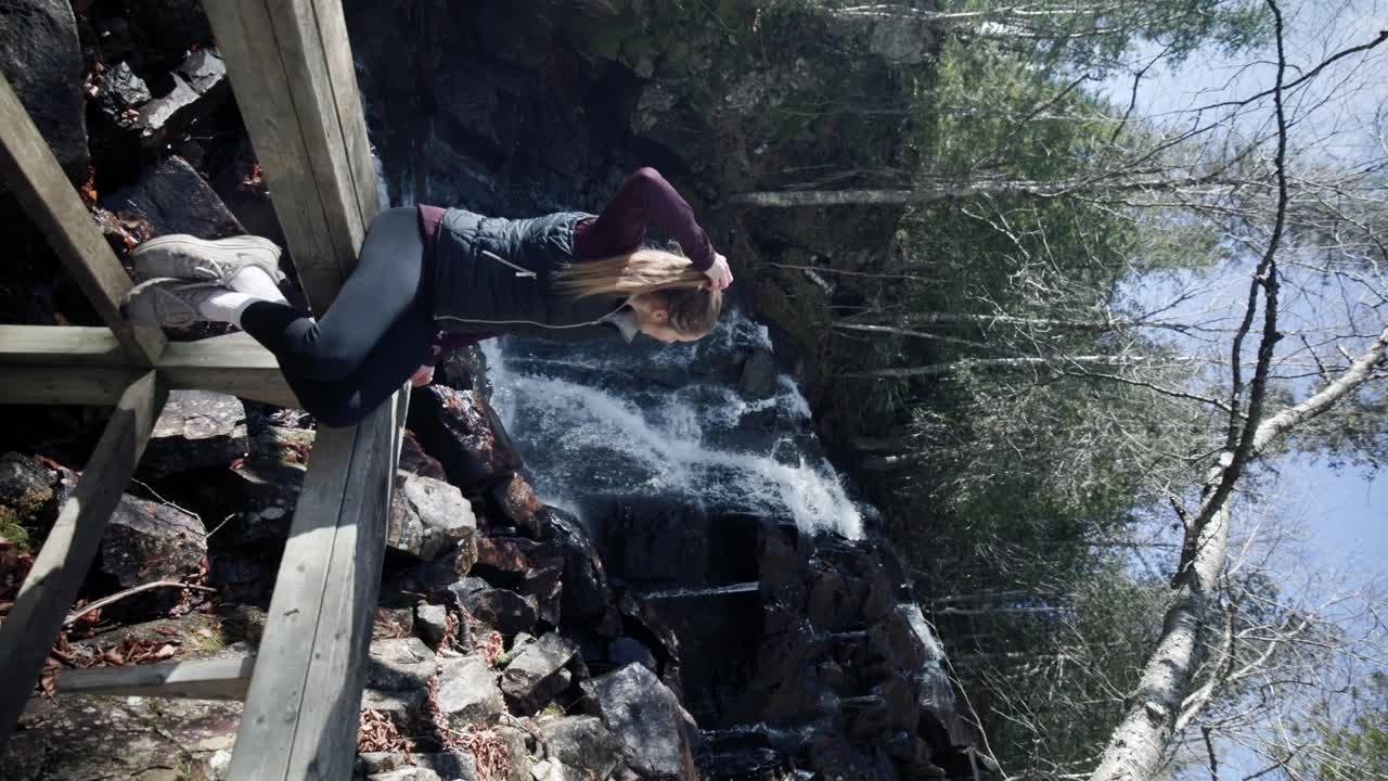 폭포를 배경으로 나무 전망대에 앉아 있는 여성의 세로 보기