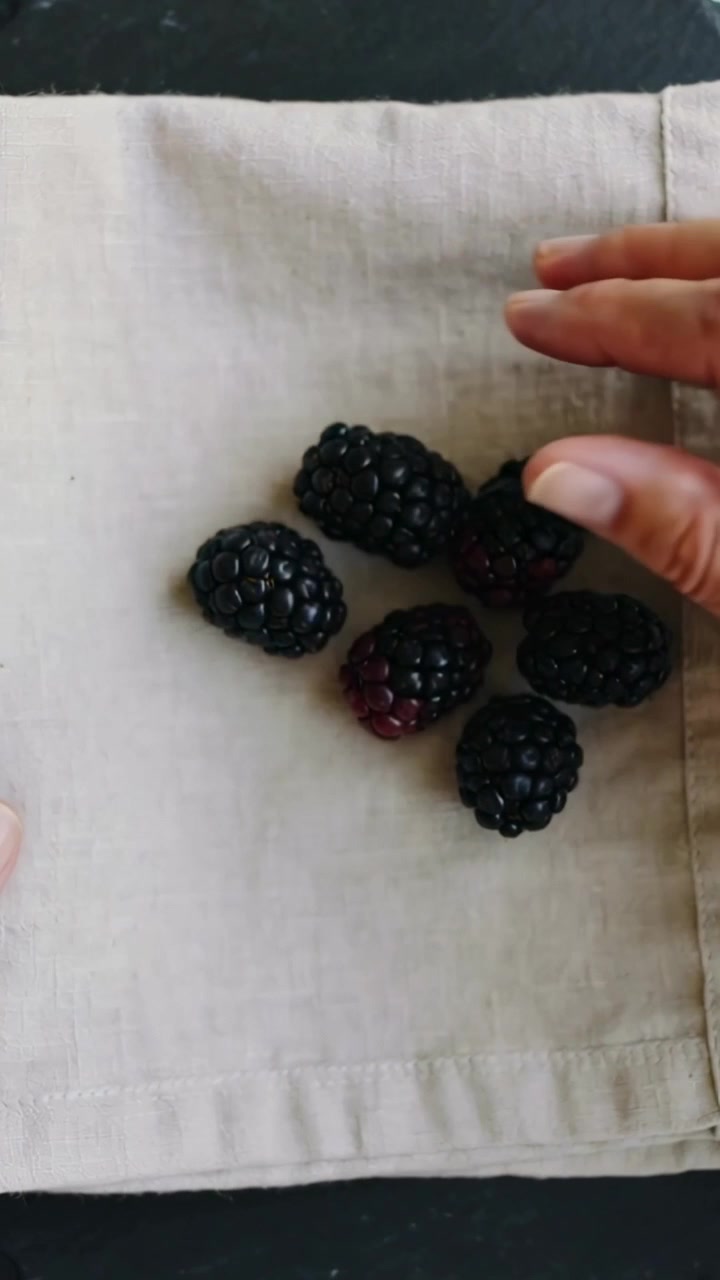 Video verticale: Un paio di mani adulte che posizionano more su un tovagliolo su un tagliere di ardesia per la composizione.