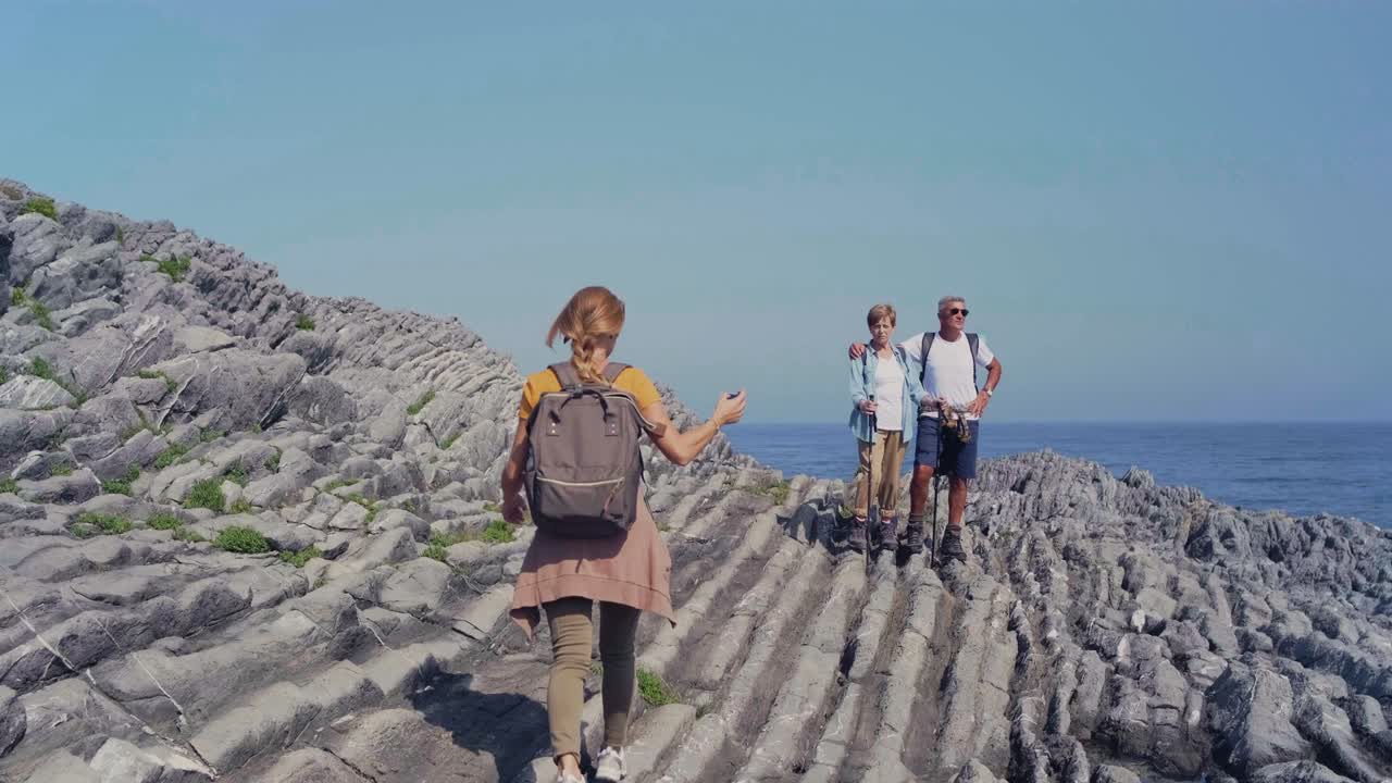 Young woman taking photo with mobile to her parents through flysch rock