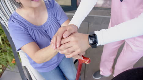 Caregiver in pink scrubs supporting senior asian woman with walking cane at home