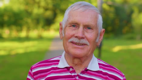 Lovely-cheerful-senior-old-gray-haired-grandfather-in-casual-red-t-shirt-on-summer-park-background