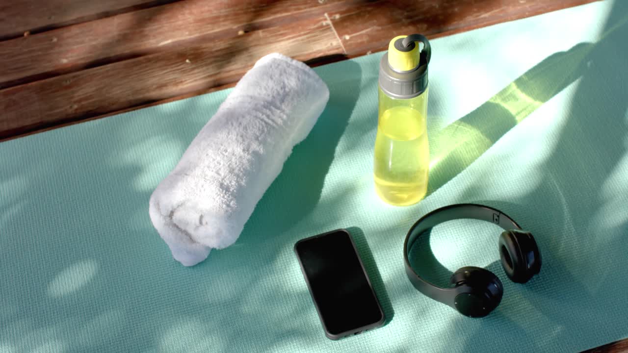 Asciugamano, bottiglia d'acqua, cuffie e smartphone su tappetino da yoga in baita, al rallentatore