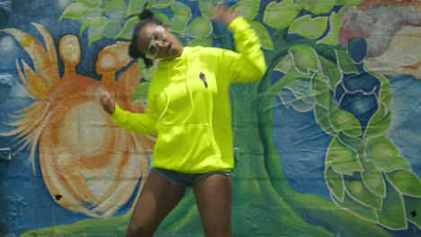 increíble coreografía de baile con una mujer joven en una sudadera con capucha verde con arte de pared en el fondo