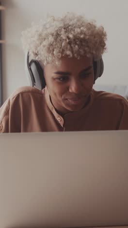young african american woman puts headphones and looking at laptop sits at desk