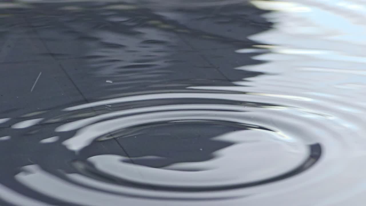 Macro shot of water droplets falling in slow motion on a garden table, creating ripples on the surface
