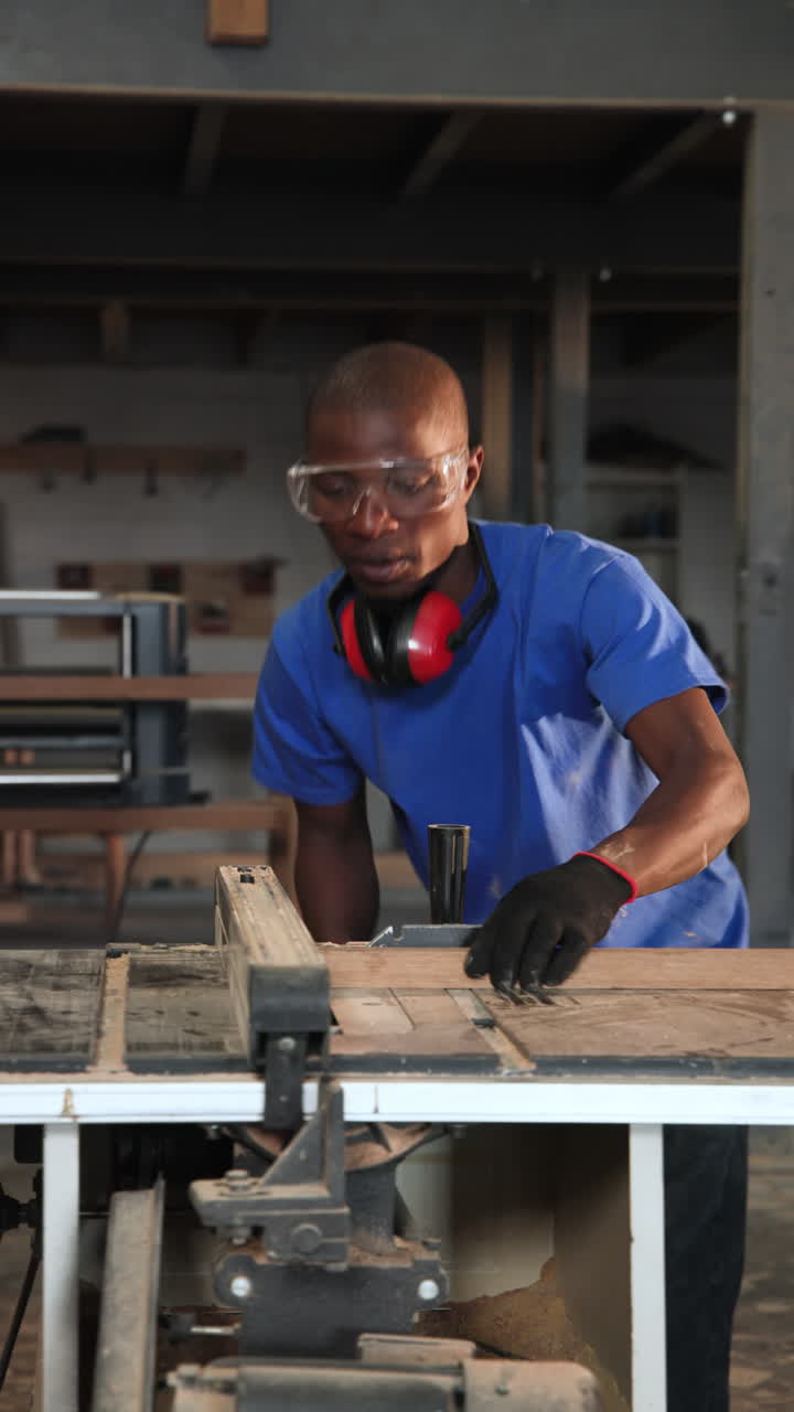 Vertical video: Hearing saw spin African American mid adult man cutting planks in shop for assembly