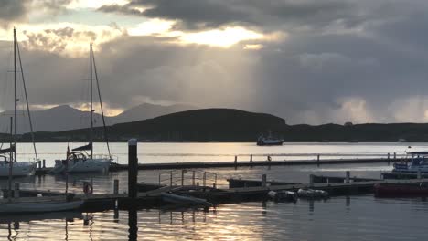 luz moteada a través de las nubes sobre un puerto tranquilo y un puerto deportivo al atardecer | oban, escocia | alta definición, 24 fps