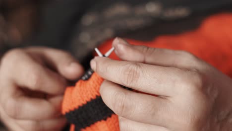 close up of woman's hands knitting with red and black thread and needle crafts