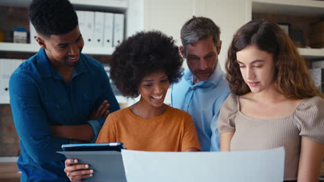 Multi-Cultural-Business-Team-Meeting-In-Office-Looking-At-Digital-Tablet-And-Documents