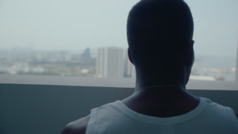 pensive black man with basketball looking at city through window