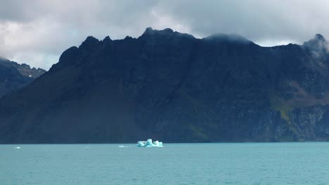 small iceberg in front of a huge mountain range on a sunny day in turquoise water