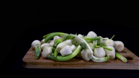 chopped onion and leaks on a wooden chopping board with black background. - panning shot right to left