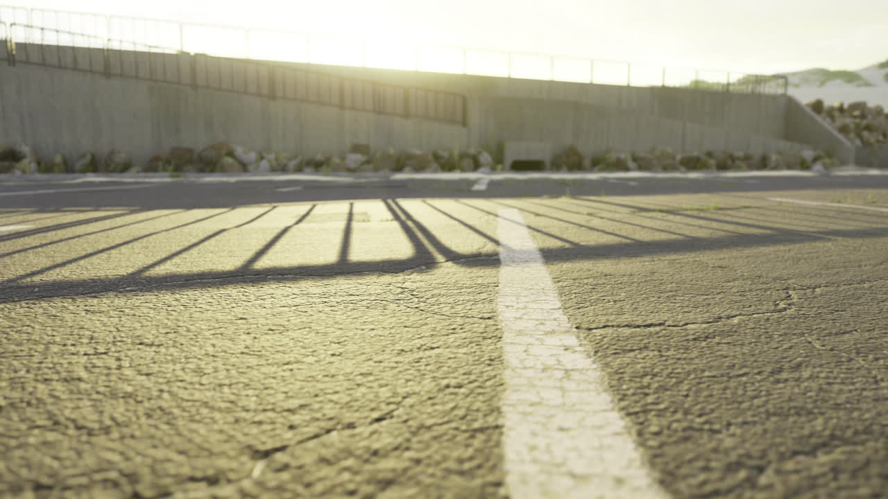 Sunrise casts long shadows over cracked pavement in an open area