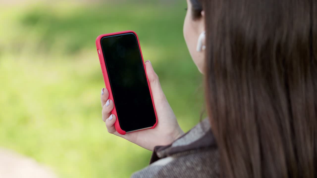 아름다운 소녀는 공원의 벤치에 앉아있는 동안 스마트폰에 소셜 네트워크의 테이프를 통해 음악을 듣고 떠납니다.