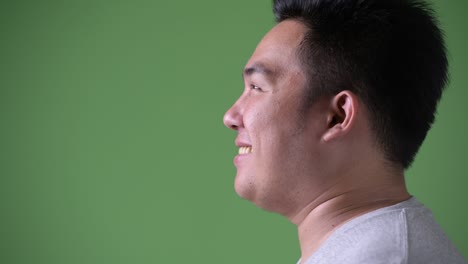 young handsome overweight asian man against green background