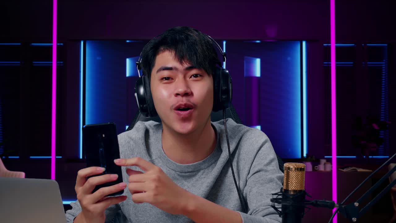 un hombre asiático sonriente con una computadora revisando un teléfono móvil en una habitación iluminada por luces de neón en retro